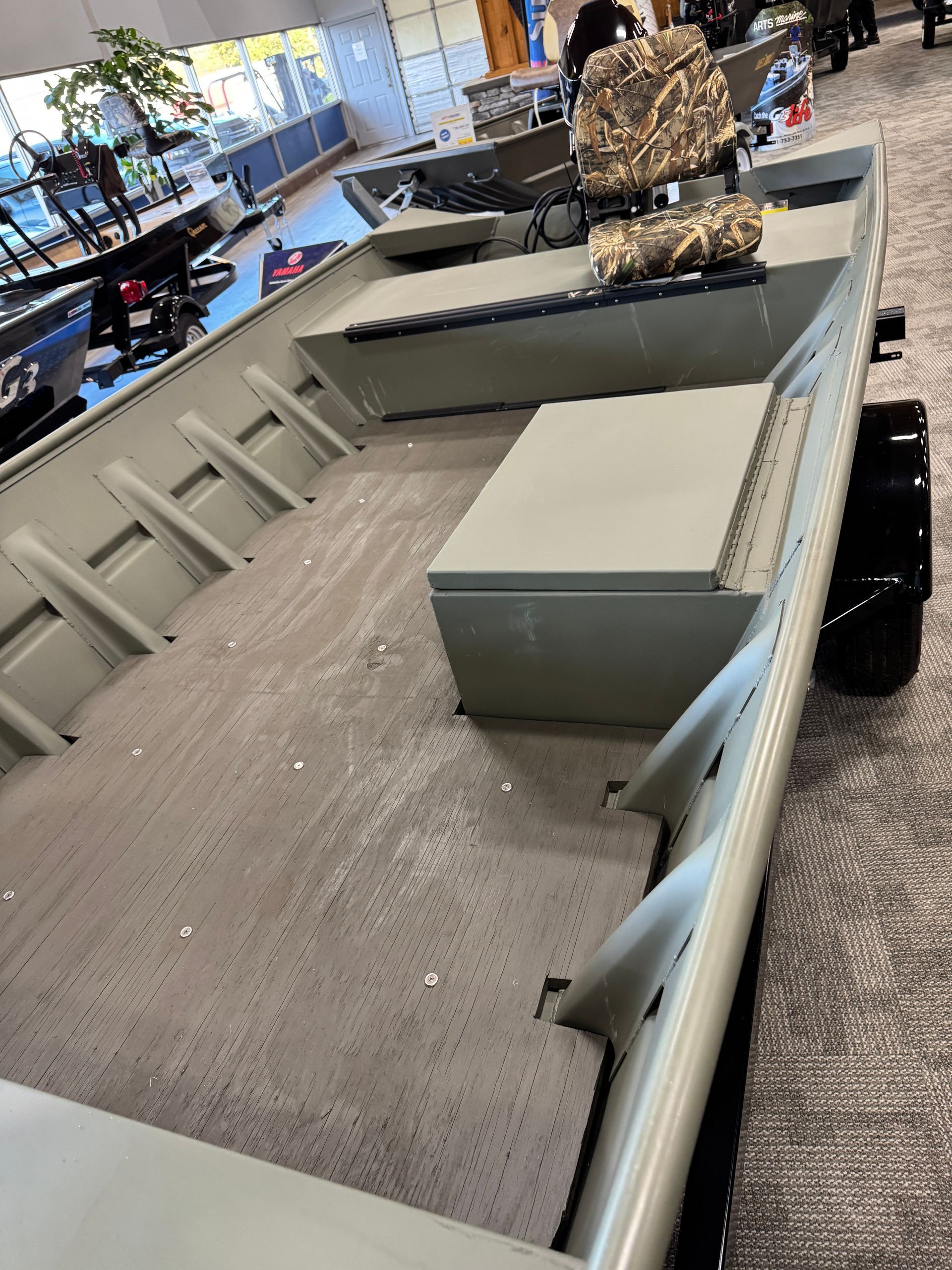 Small gray boat interior with bench seats and a person in camouflage standing inside a showroom or exhibit