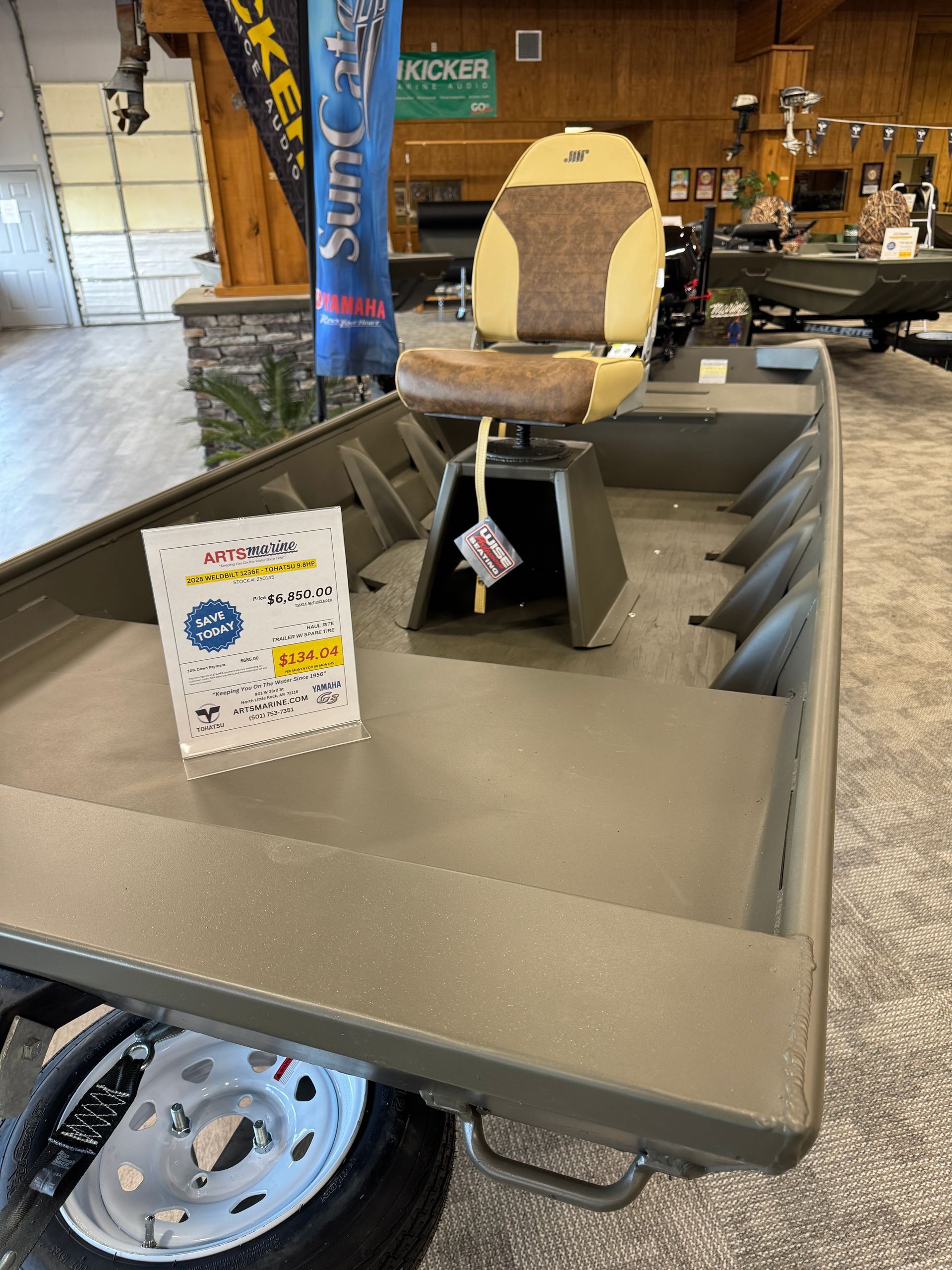 Close-up of a beige utility cart with shelves, a sign, and a chair in a workshop or showroom setting