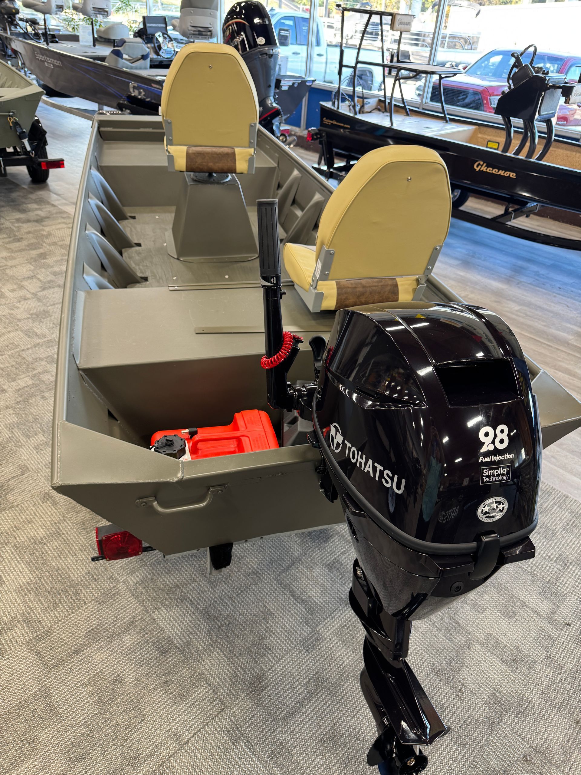 Small gray fishing boat with beige seats and a black outboard motor on display indoors.
