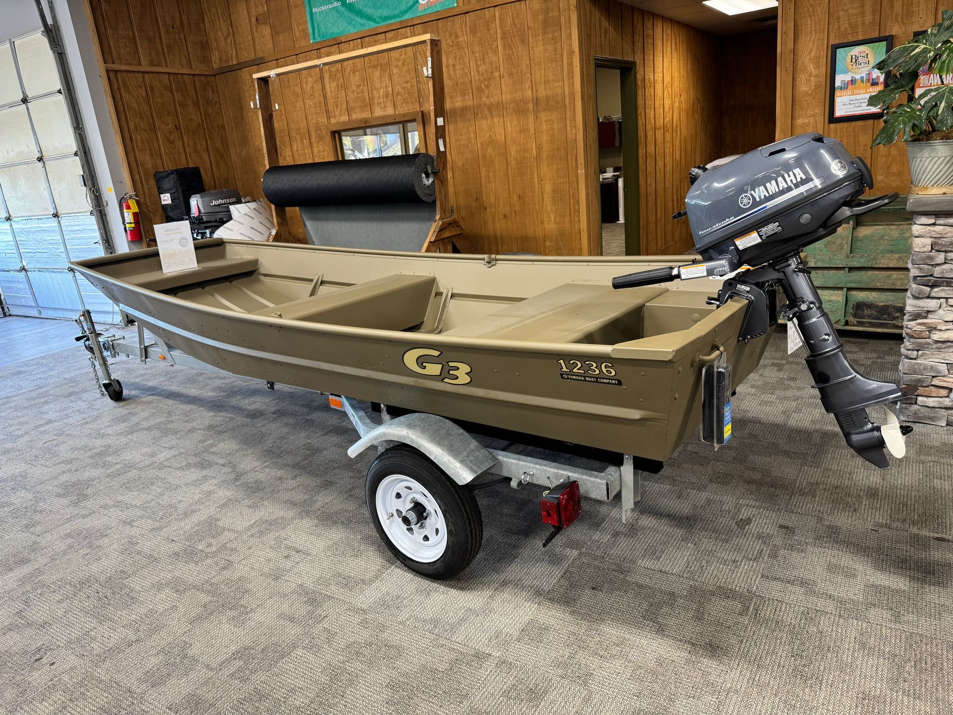 Tan G3 jon boat with motor and trailer, inside a dealership.