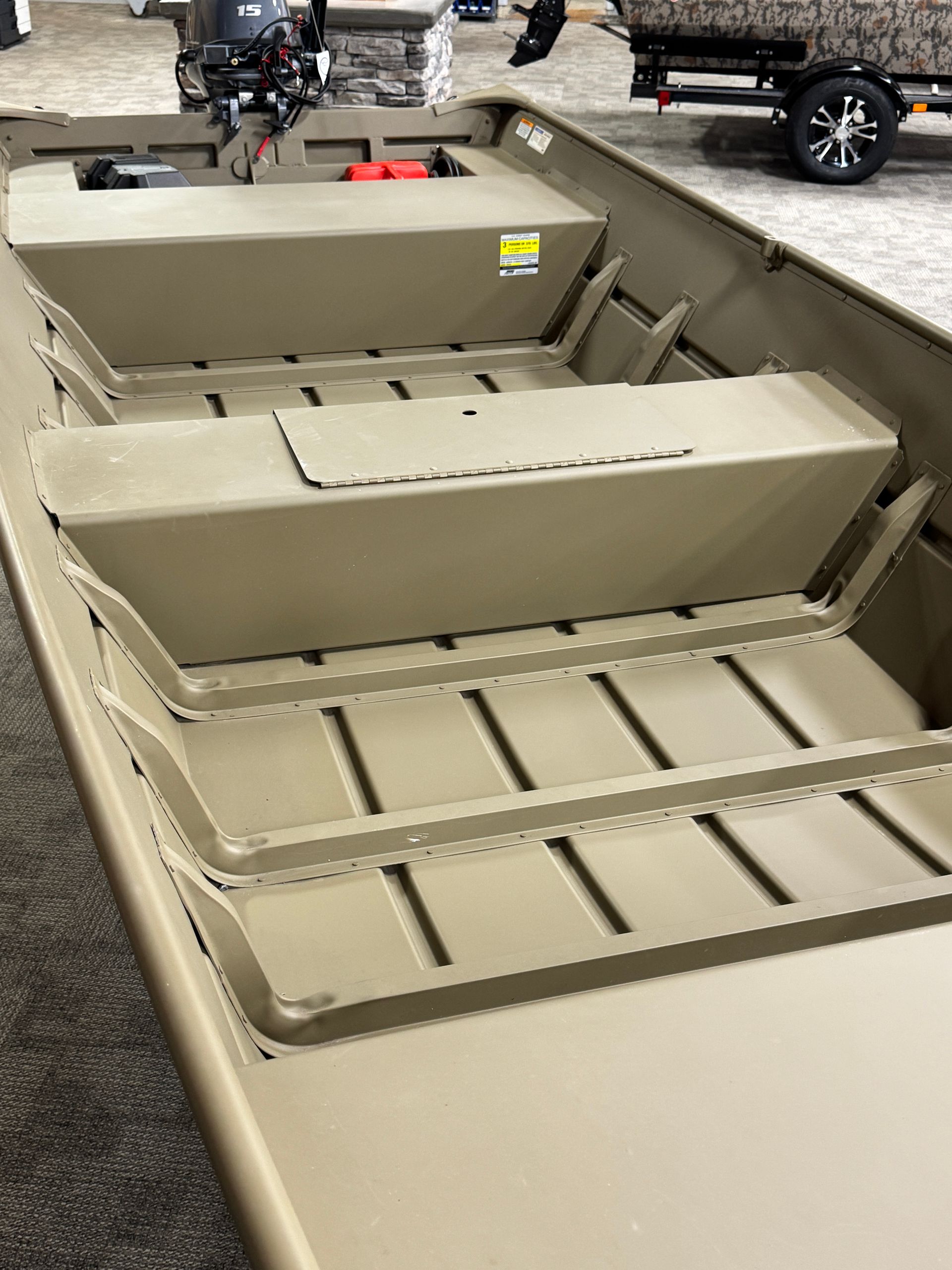 Small beige metal fishing boat with bench seats and deck storage on a trailer outdoors