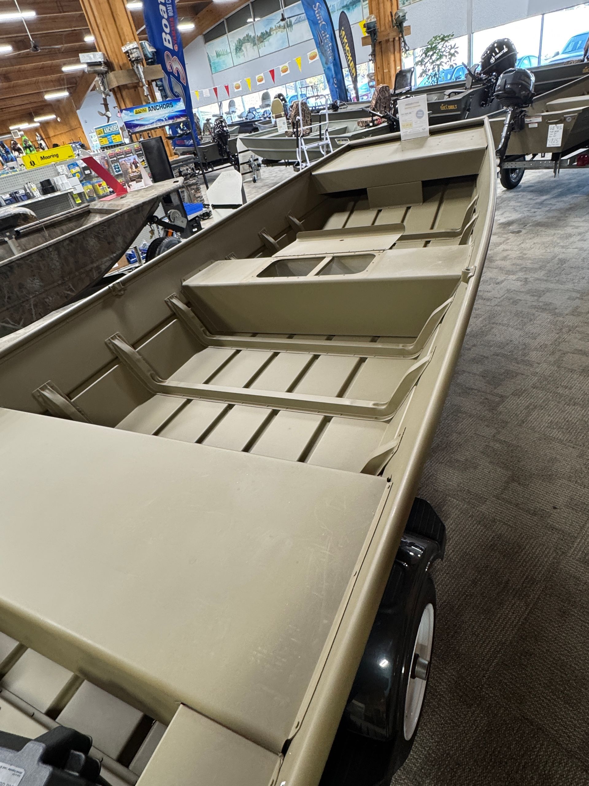 Tan military utility trailer with open cargo bed in an indoor showroom, angled view.