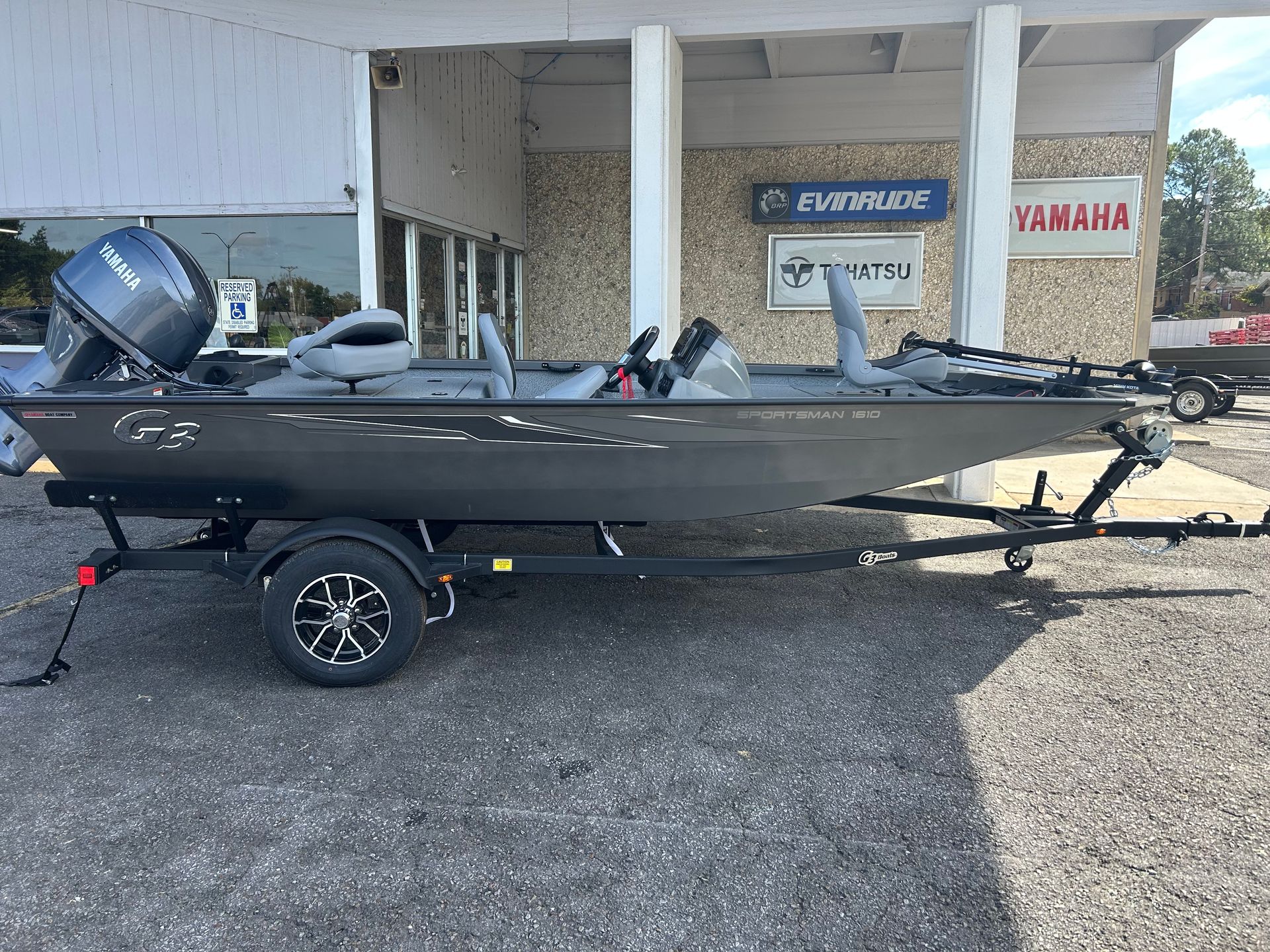 Black fishing boat on trailer parked outside a store with Yamaha sign and outboard motor