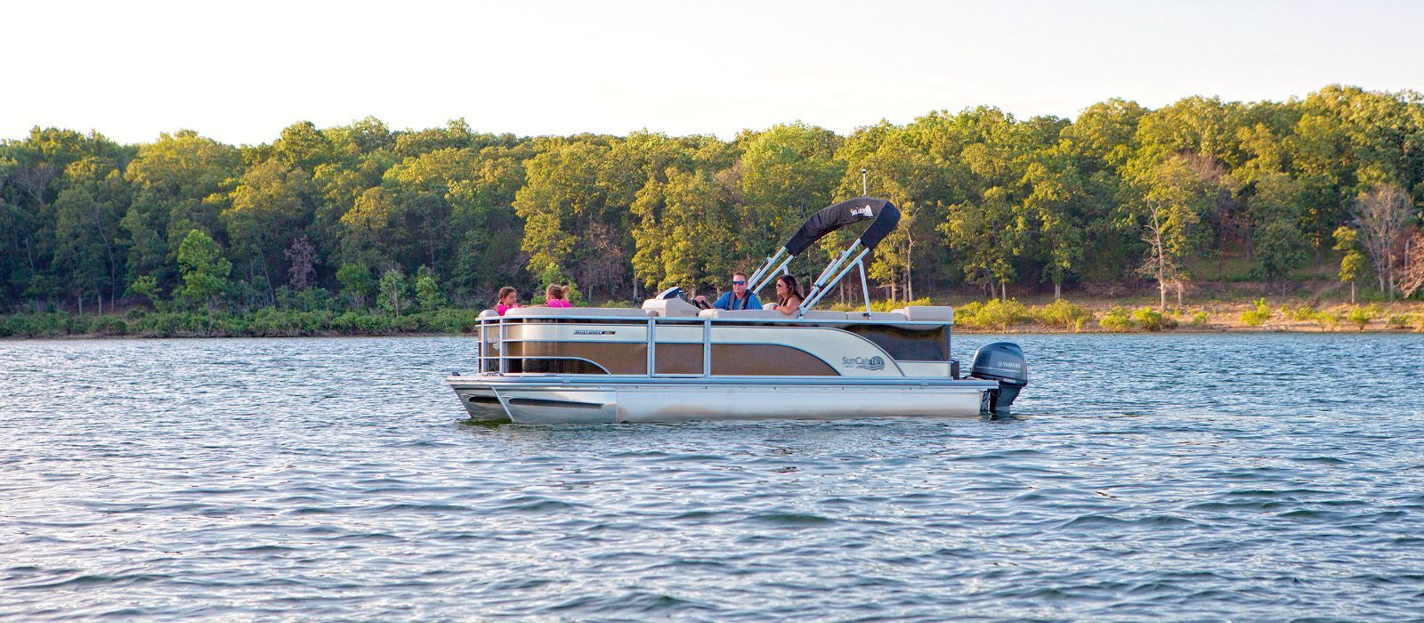 A pontoon boat is floating on top of a lake surrounded by trees.