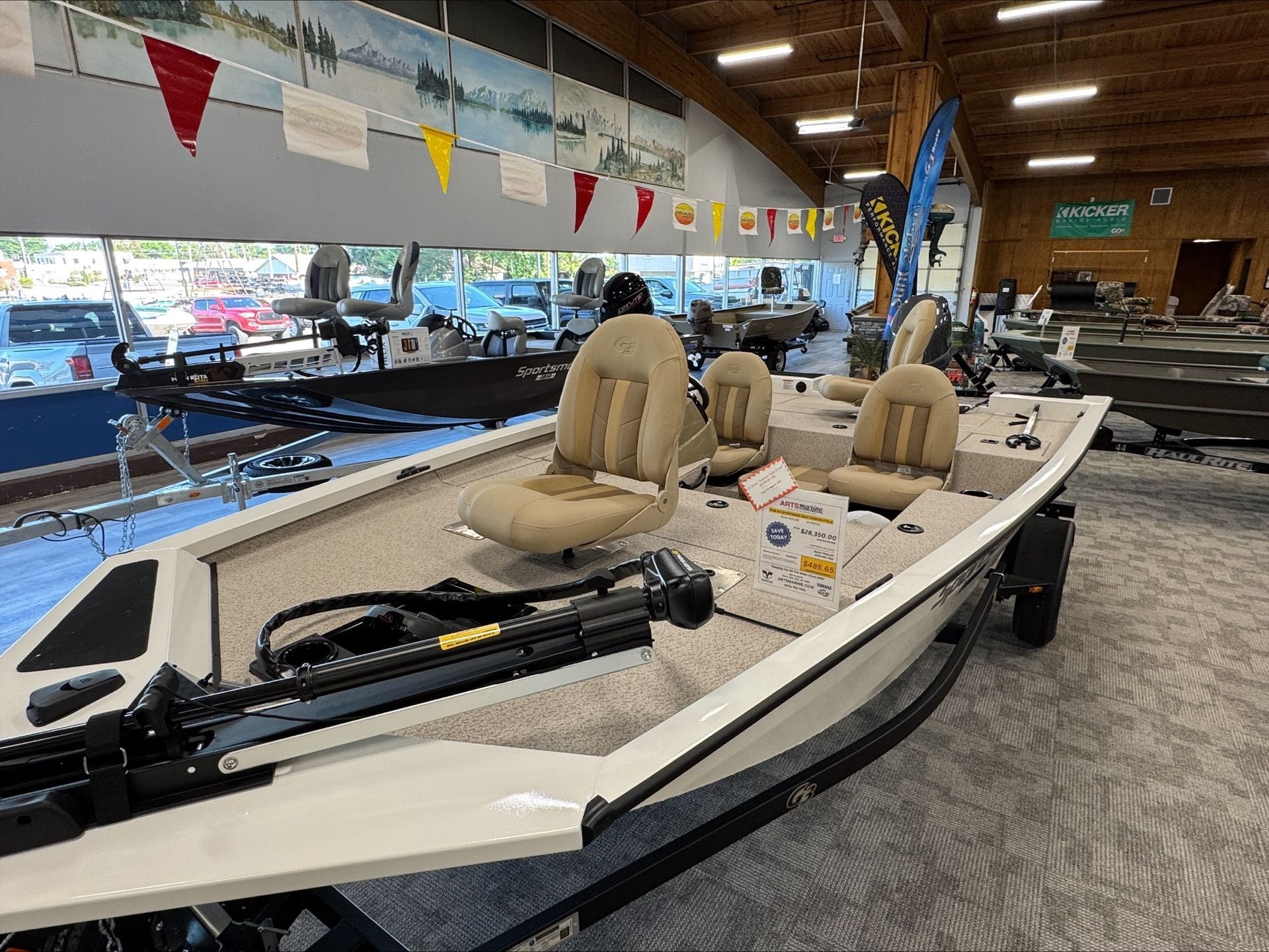 Tan fishing boat on display inside a building with other boats and outdoor scene murals.