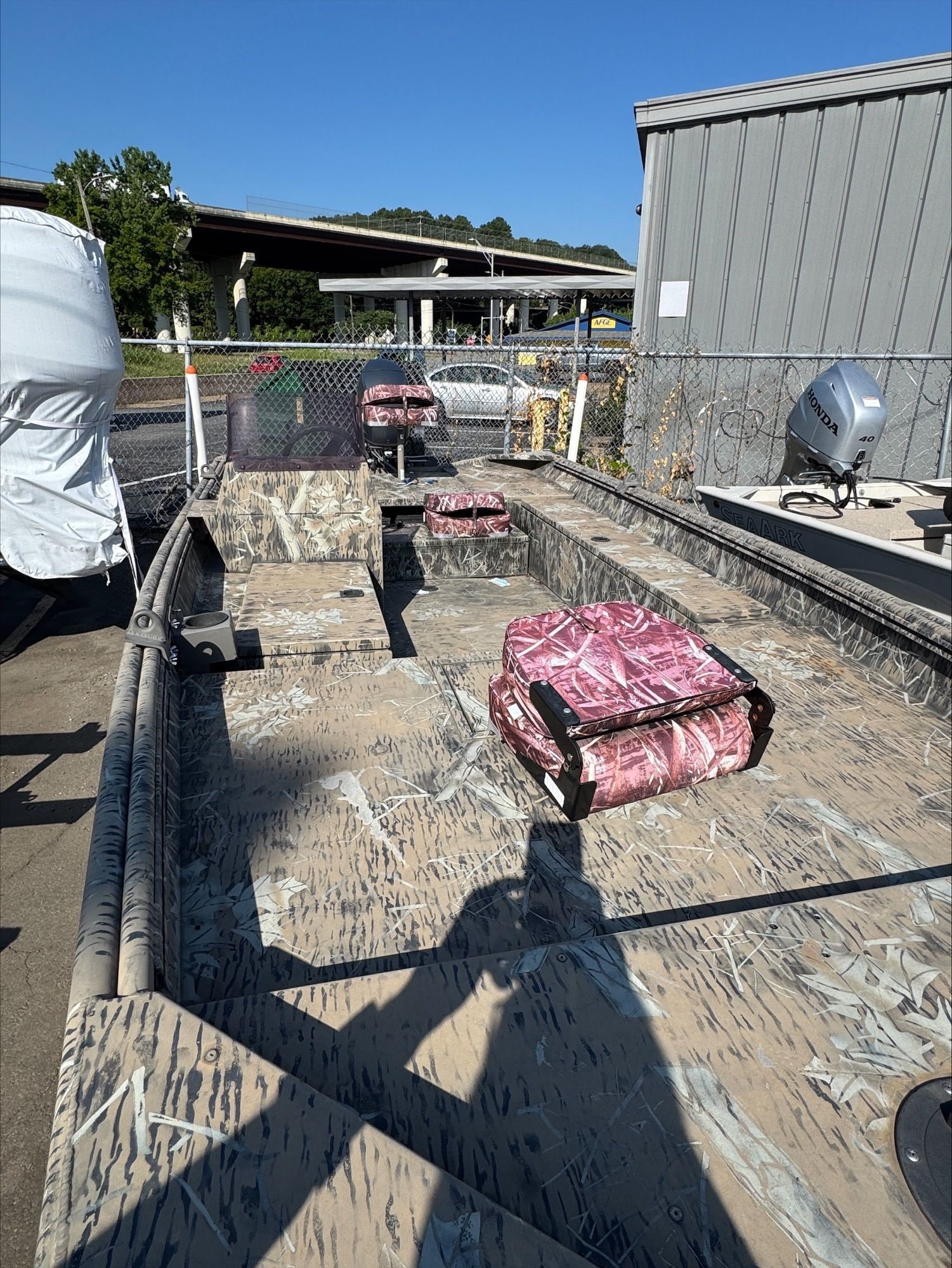 Camouflage boat with a pink object inside. Outdoors, sunny.