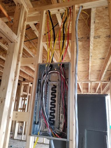 Open electrical panel with wires inside a framed wall during house construction.