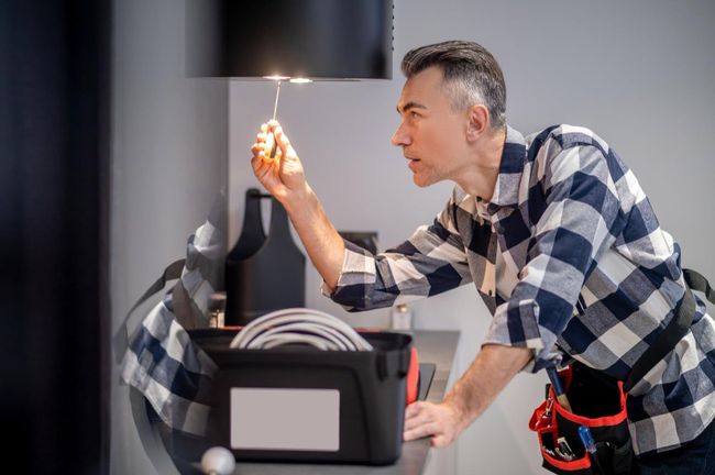 Man in plaid shirt using a handheld torch to repair a black appliance on a countertop
