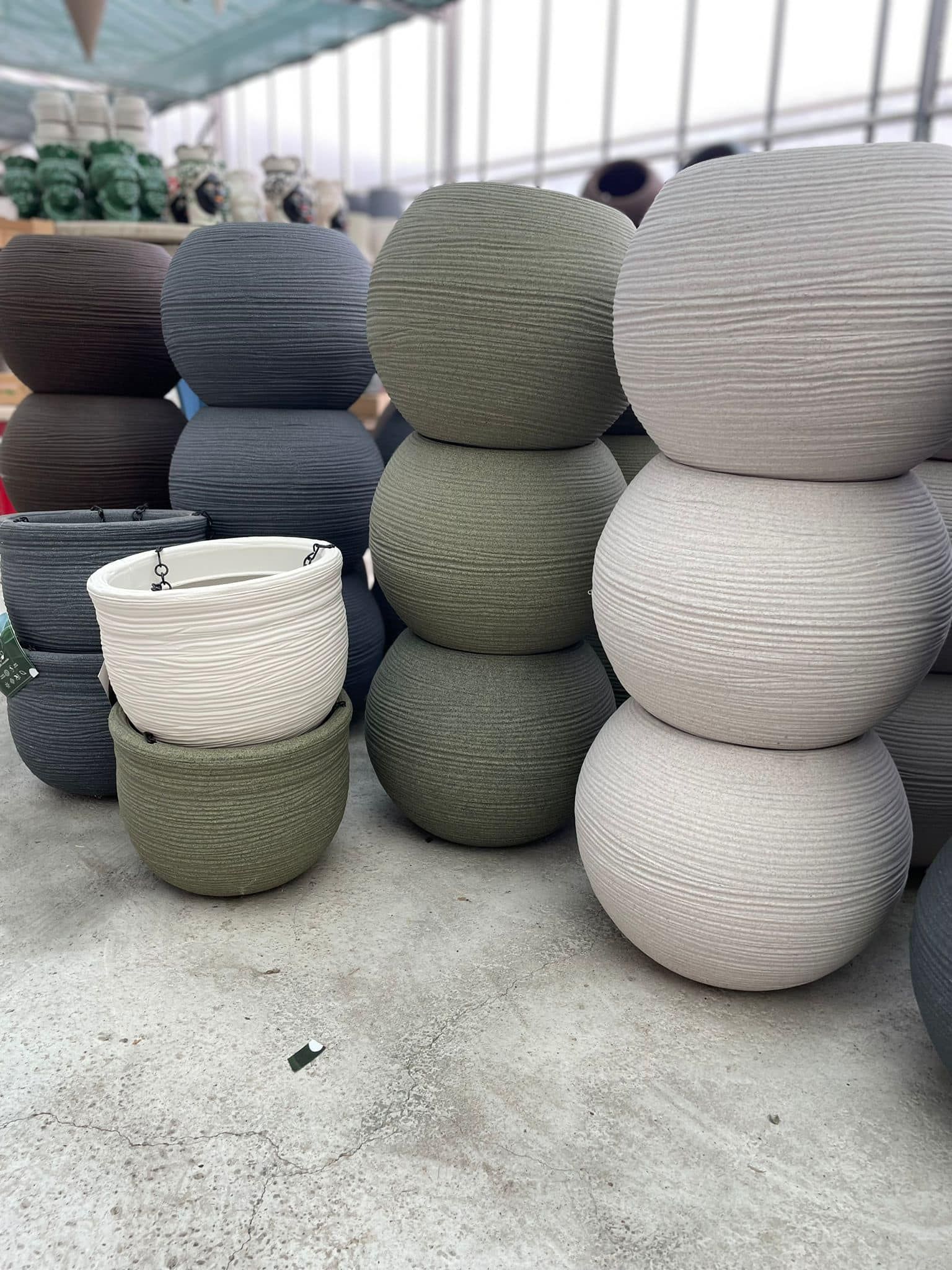 Pile di grandi vasi intrecciati di colore grigio, bianco e verde, disposti in una bancarella di un mercato all'aperto.