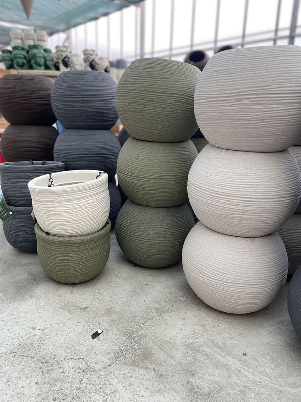 Vasi rotondi intrecciati, impilati nei colori grigio, bianco e verde, su un pavimento di cemento in un corridoio di un mercato o di un magazzino.