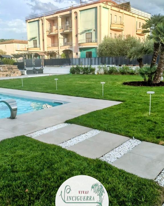 Prato e vialetto a bordo piscina di fronte a un condominio beige con balconi.