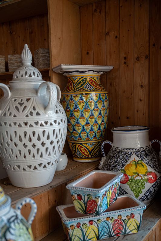 Vaschette in ceramica colorate e vasi decorati assortiti, esposti su una mensola di legno.