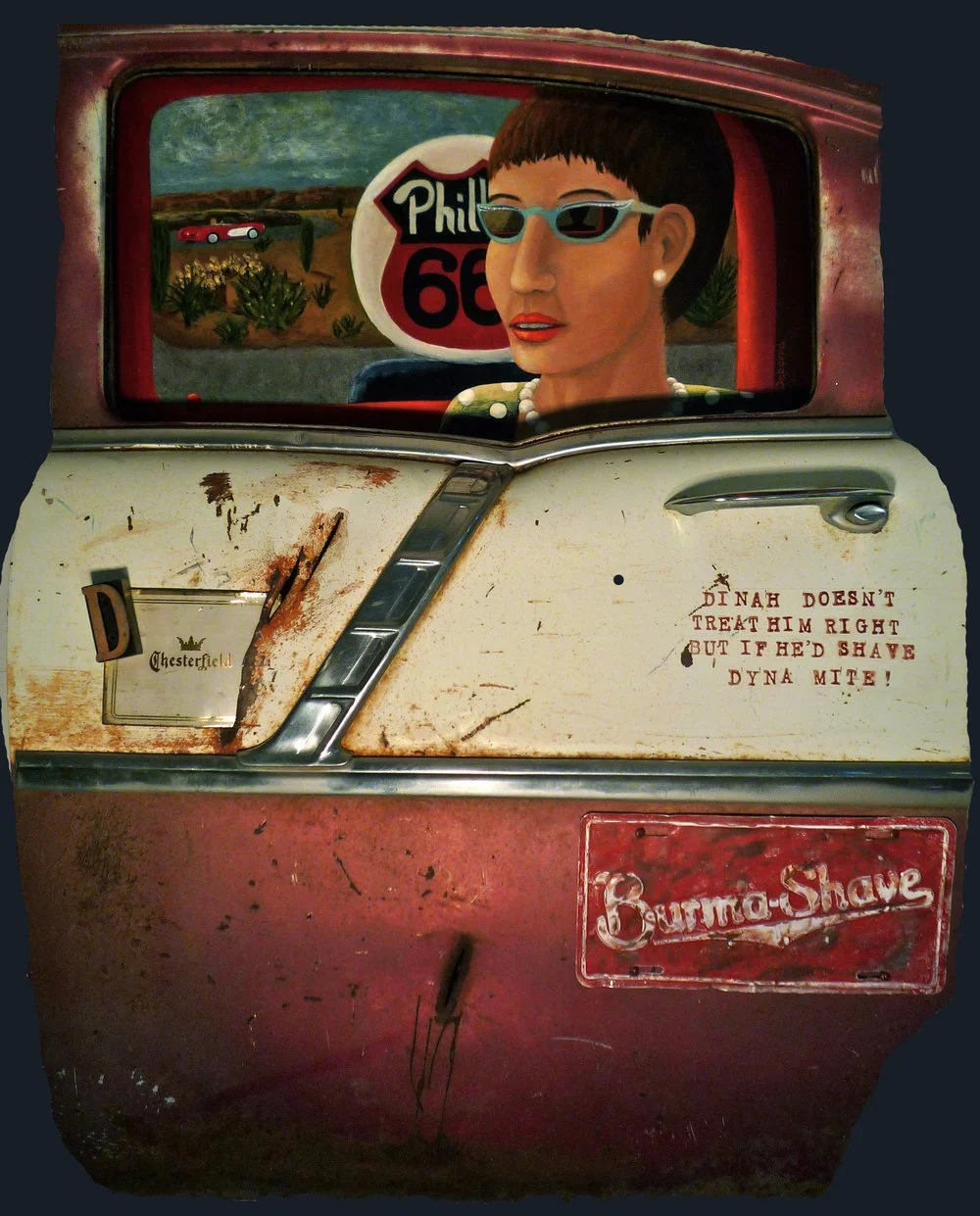 A woman in sunglasses drives a rusted car. Route 66 sign is visible in the window. The car door reads 