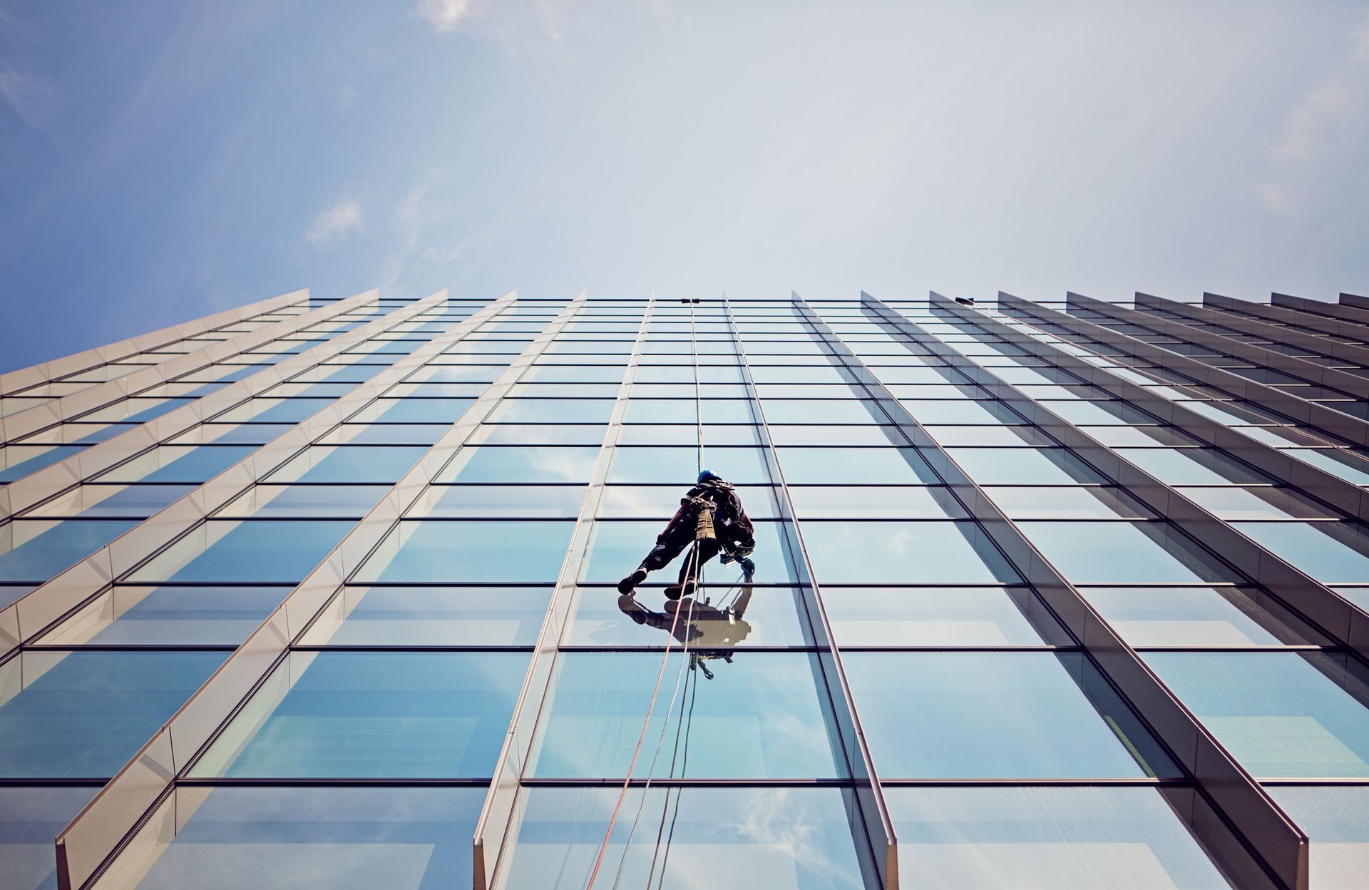 Window washer cleaning the glass facade of a tall modern building.