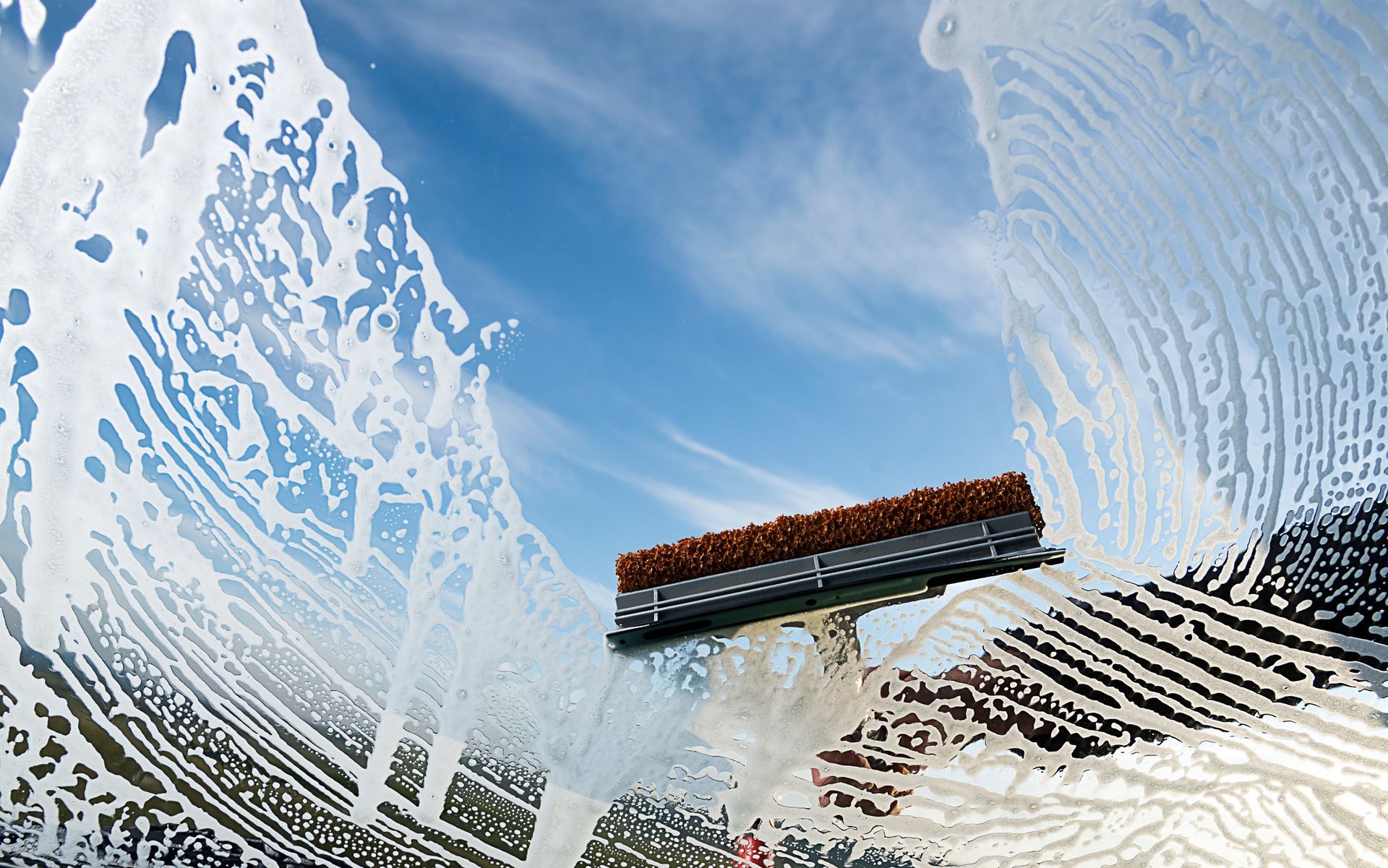 Window being cleaned with a squeegee against a bright blue sky.