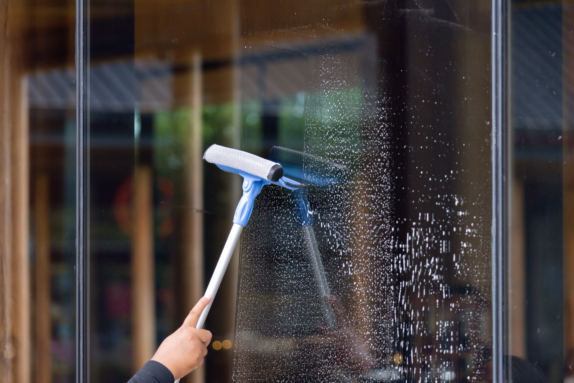 Person using a squeegee to clean a glass window.