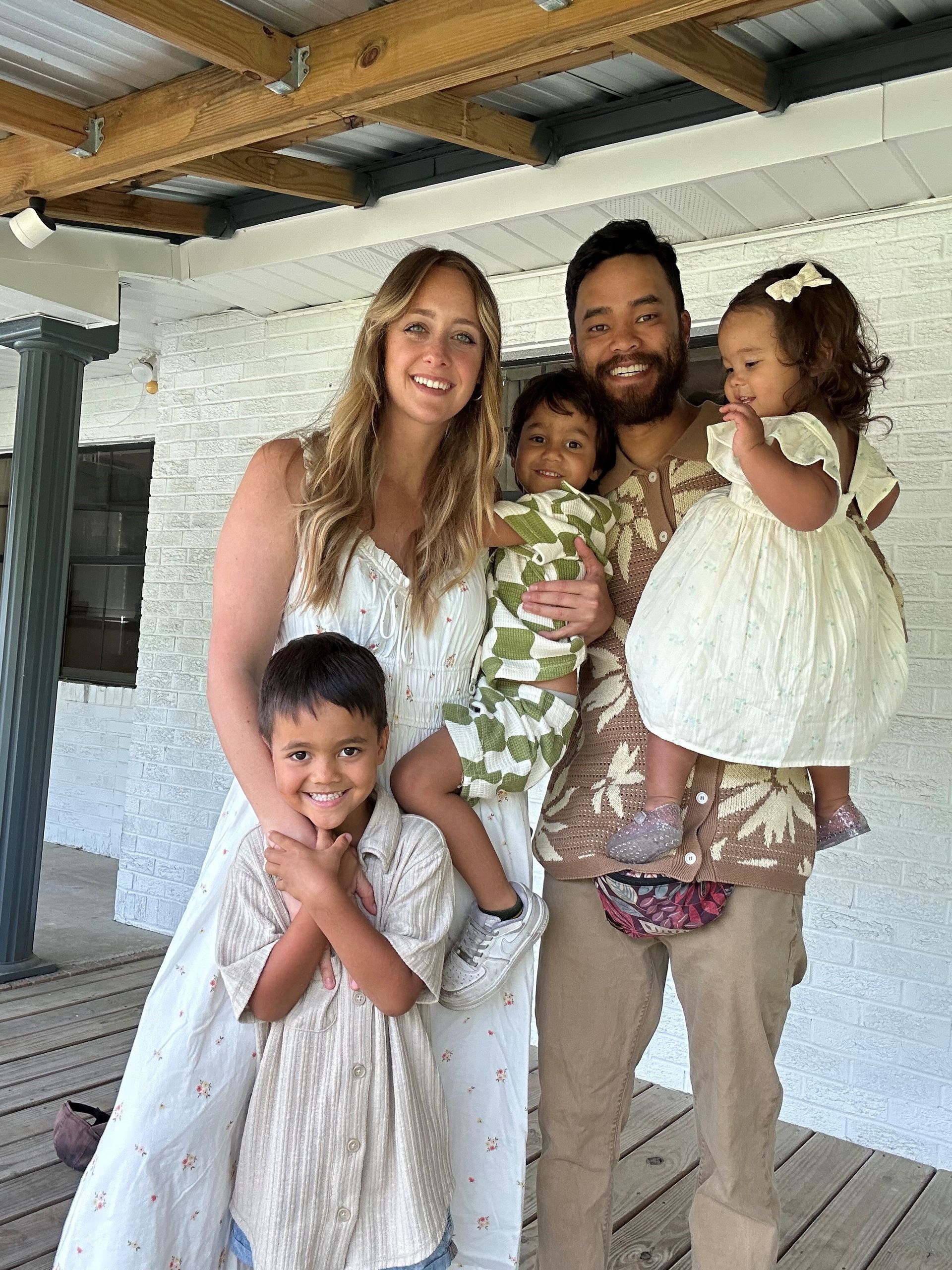 Family portrait smiling, standing on a porch. Mother, father, and three children.
