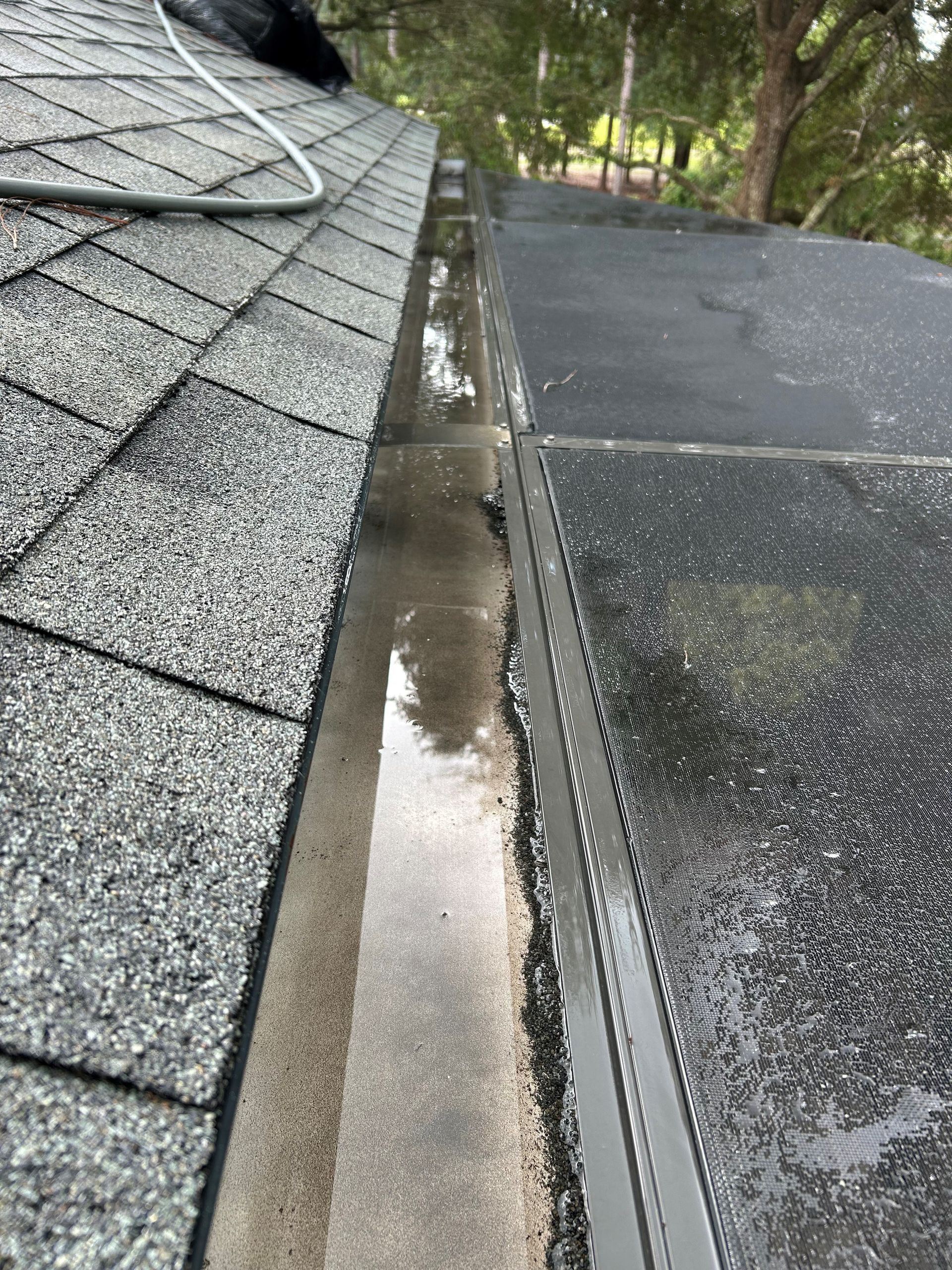 Gutter filled with water next to a shingled roof and a flat, black roof.