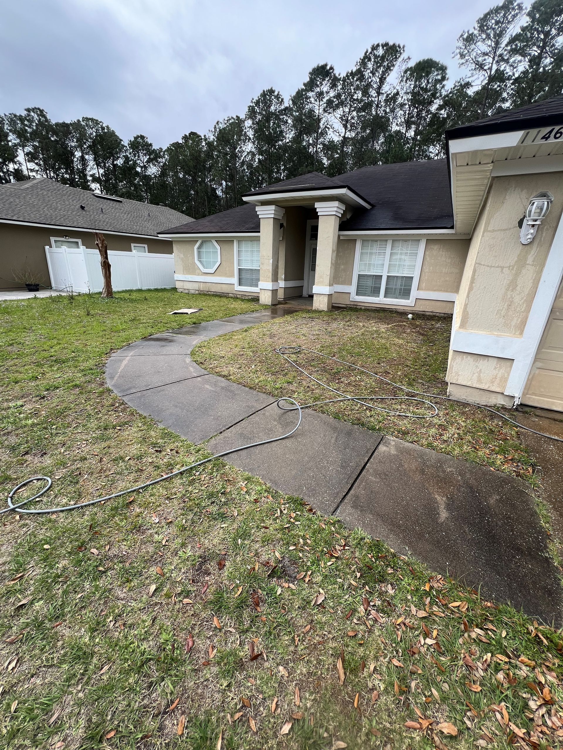 Tan house with a curved walkway; dead grass, cloudy sky.
