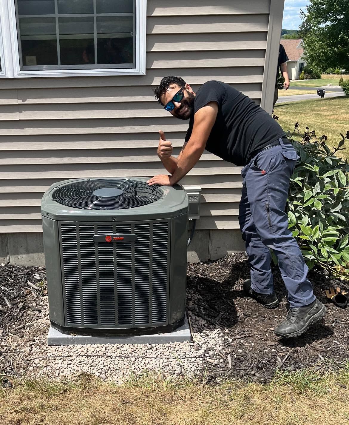 Person kneels beside an outdoor air conditioner, working on it beside a house.