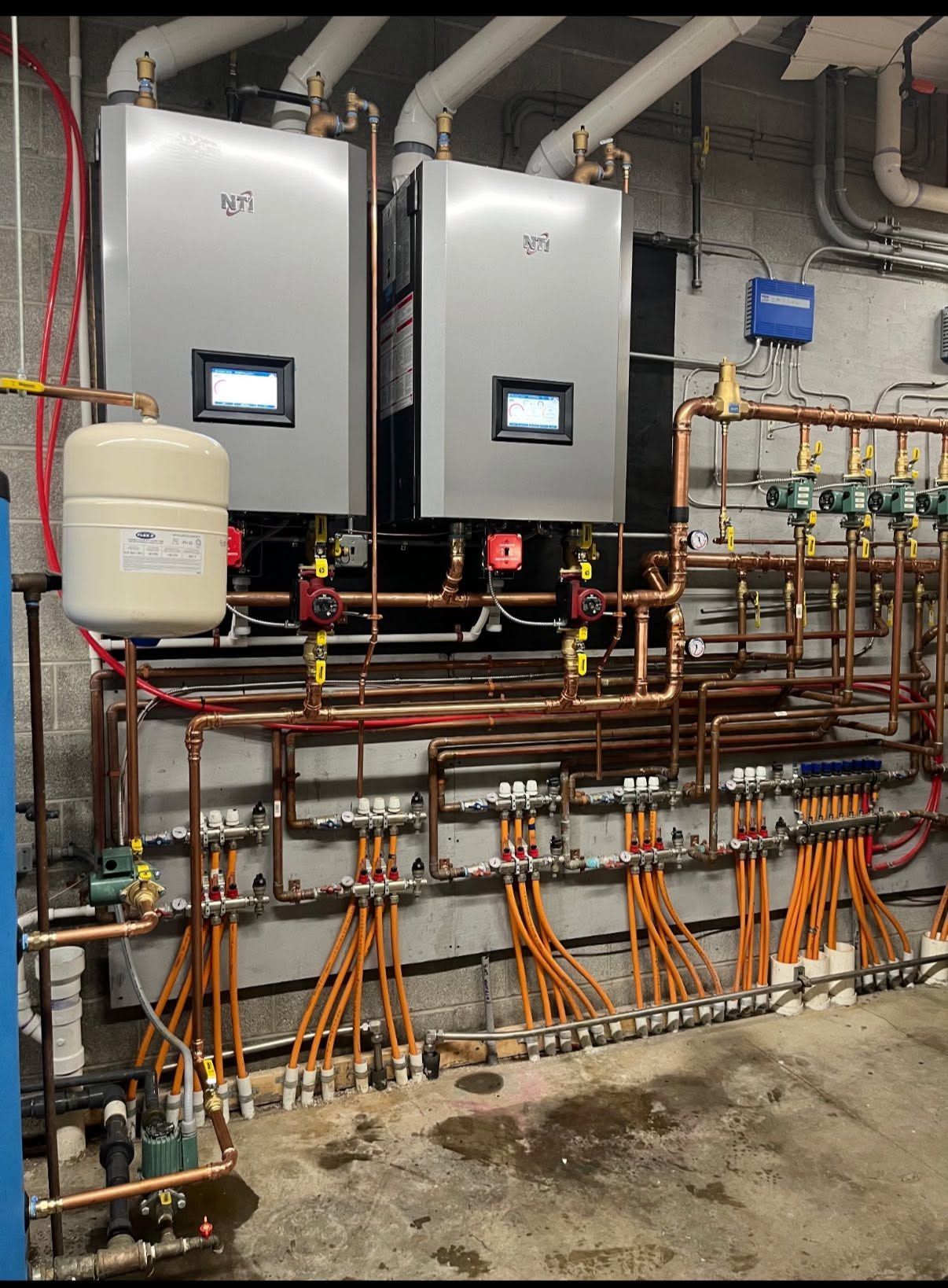 Mechanical room with two wall-mounted boilers and extensive copper piping and valves below.