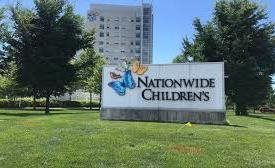Nationwide Children’s hospital sign on a grassy lawn with trees and a building behind it.