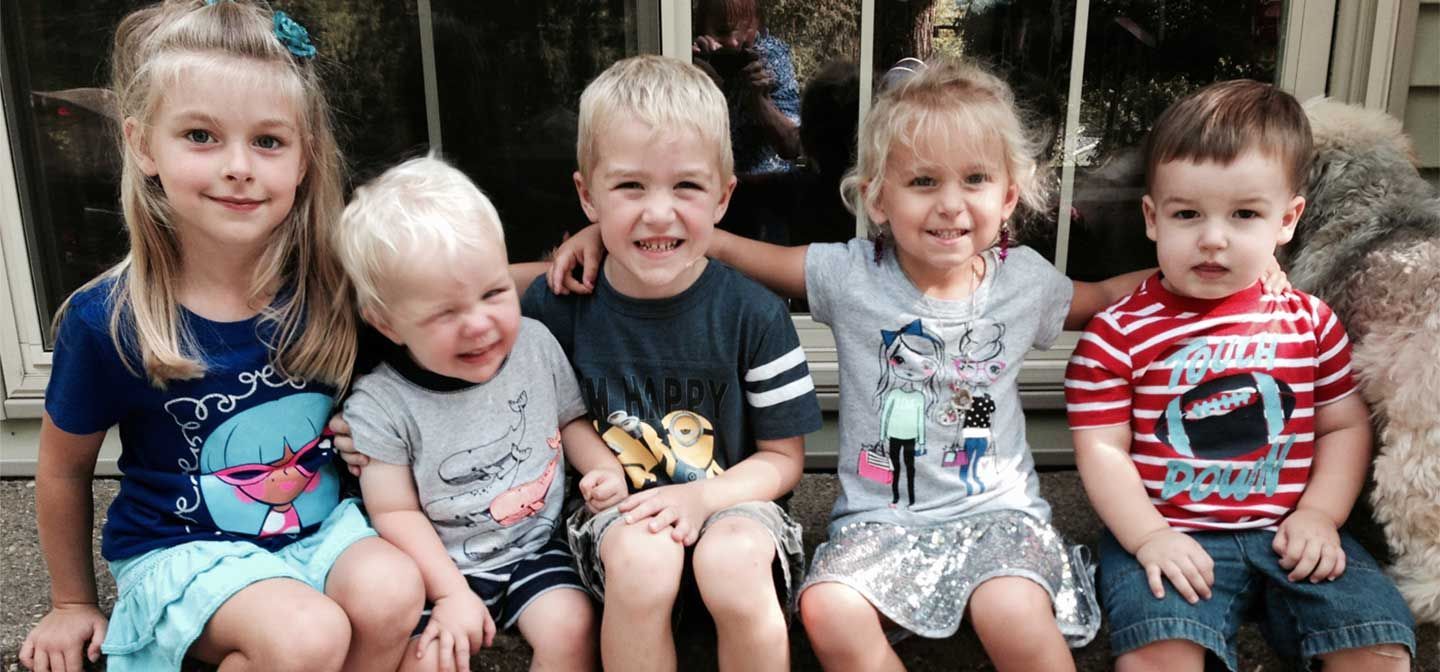 Five children sitting together outdoors, smiling at the camera.