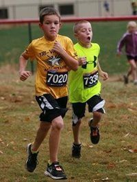 Two children running in a cross-country race, wearing yellow and neon green shirts with race numbers.