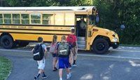 Yellow school bus stopped on a road while three students with backpacks walk toward it