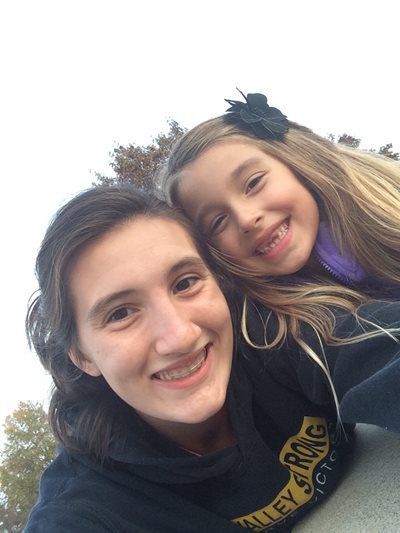 Two smiling friends leaning together outdoors, with trees in the background.
