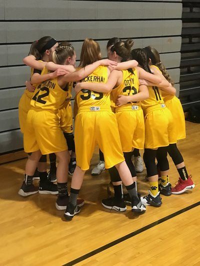 Youth basketball team in yellow huddles on a gym floor before the game.