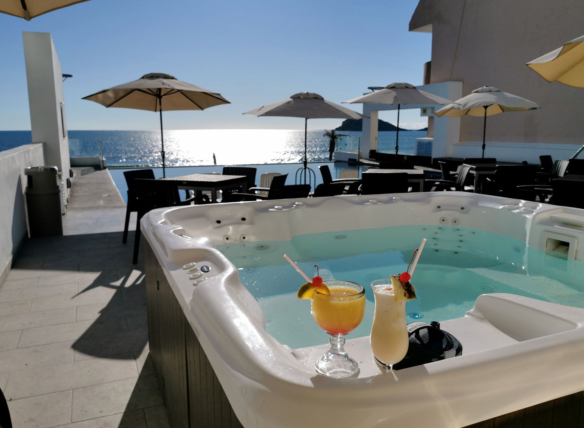 Un jacuzzi con dos bebidas y sombrillas al fondo.
