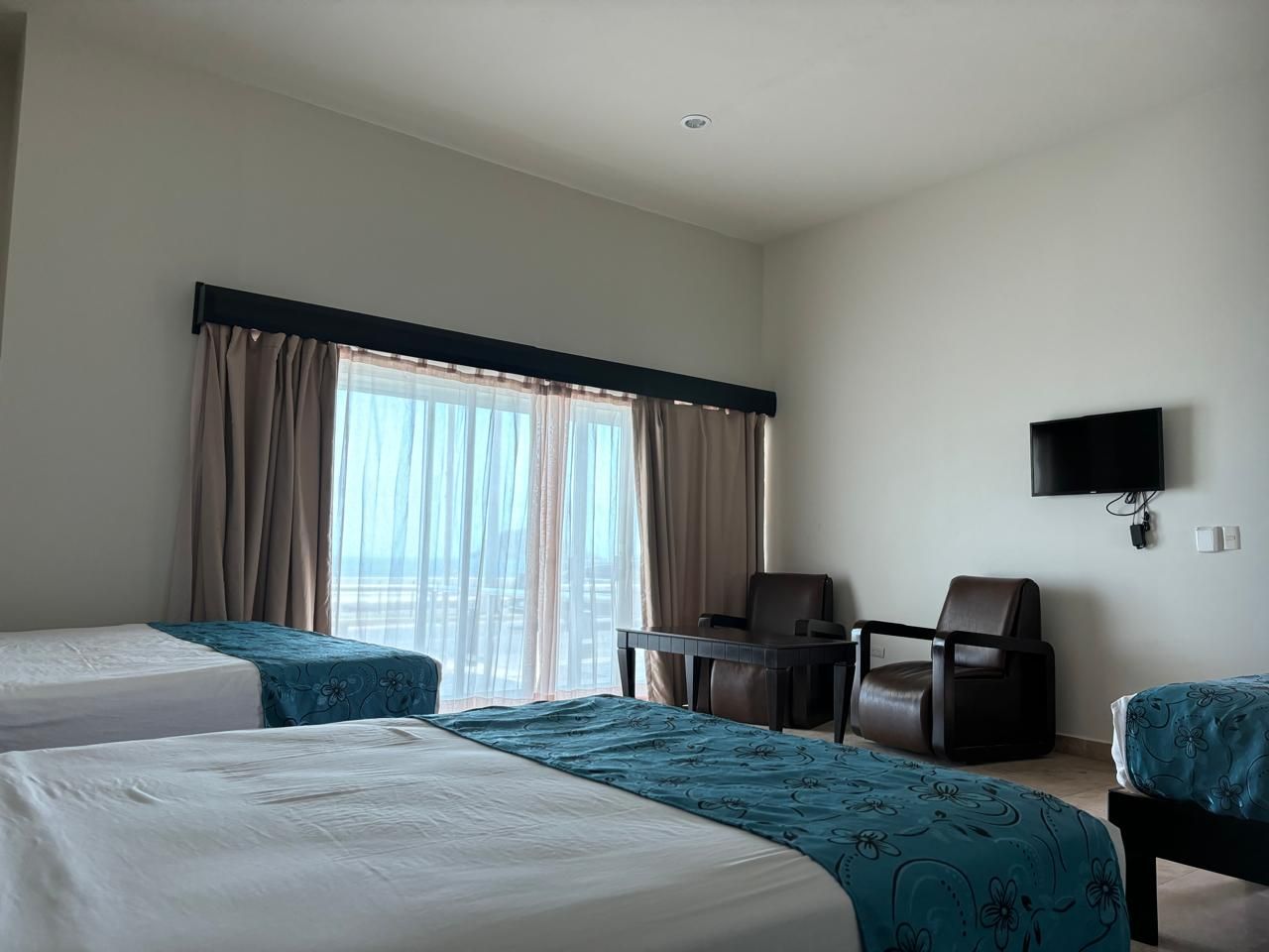 Una habitación de hotel en mazatlan sinaloa con dos camas, dos sillas y un televisor.
