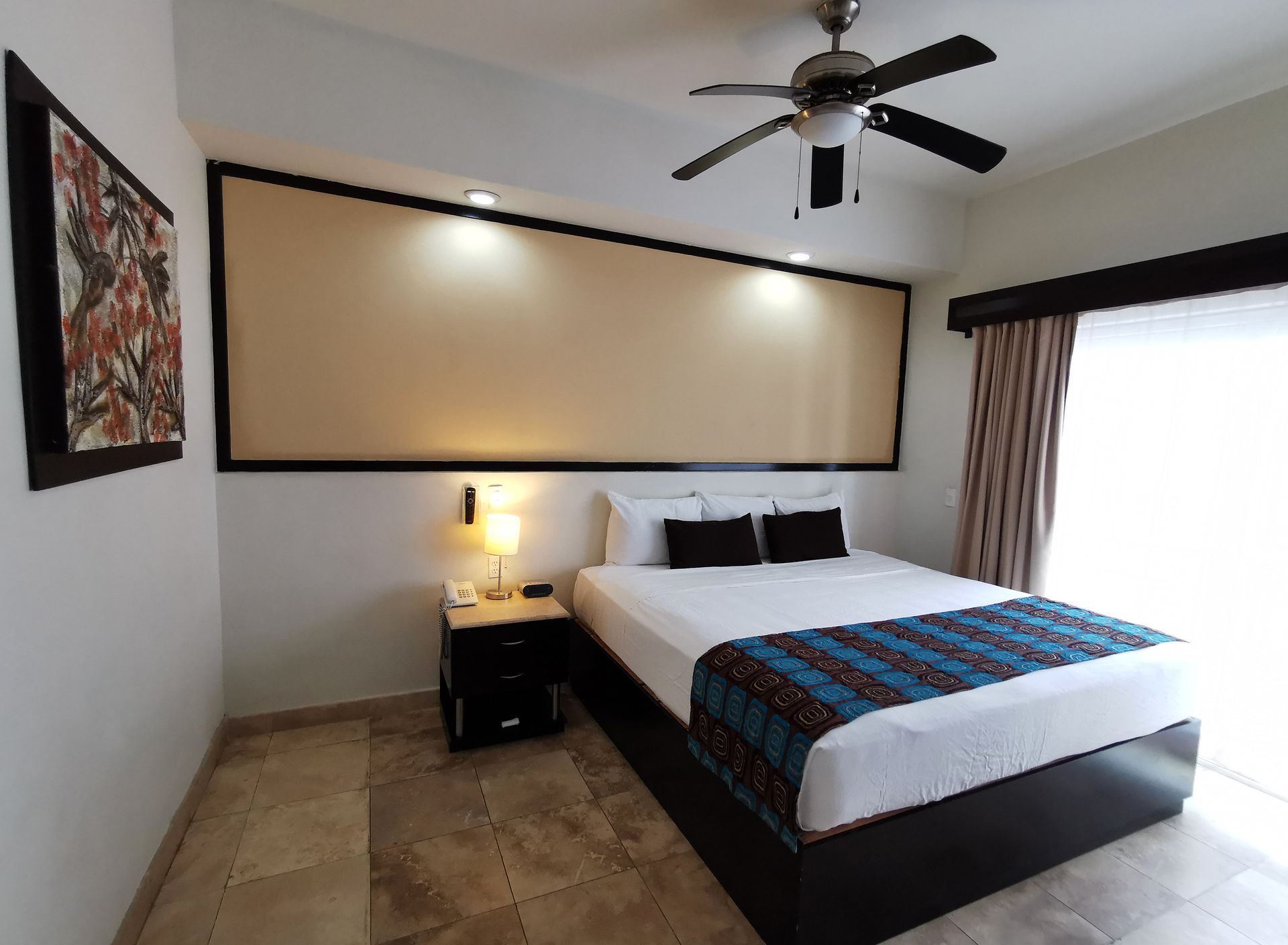 A hotel room with a king size bed and a ceiling fan