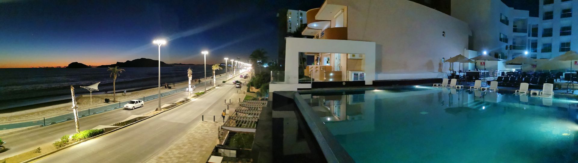 Una gran piscina está rodeada de un edificio y una playa por la noche.