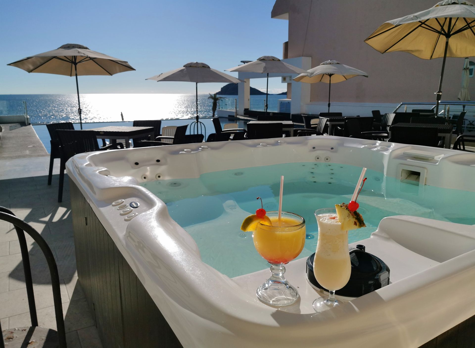 A hot tub with two drinks in it and umbrellas in the background