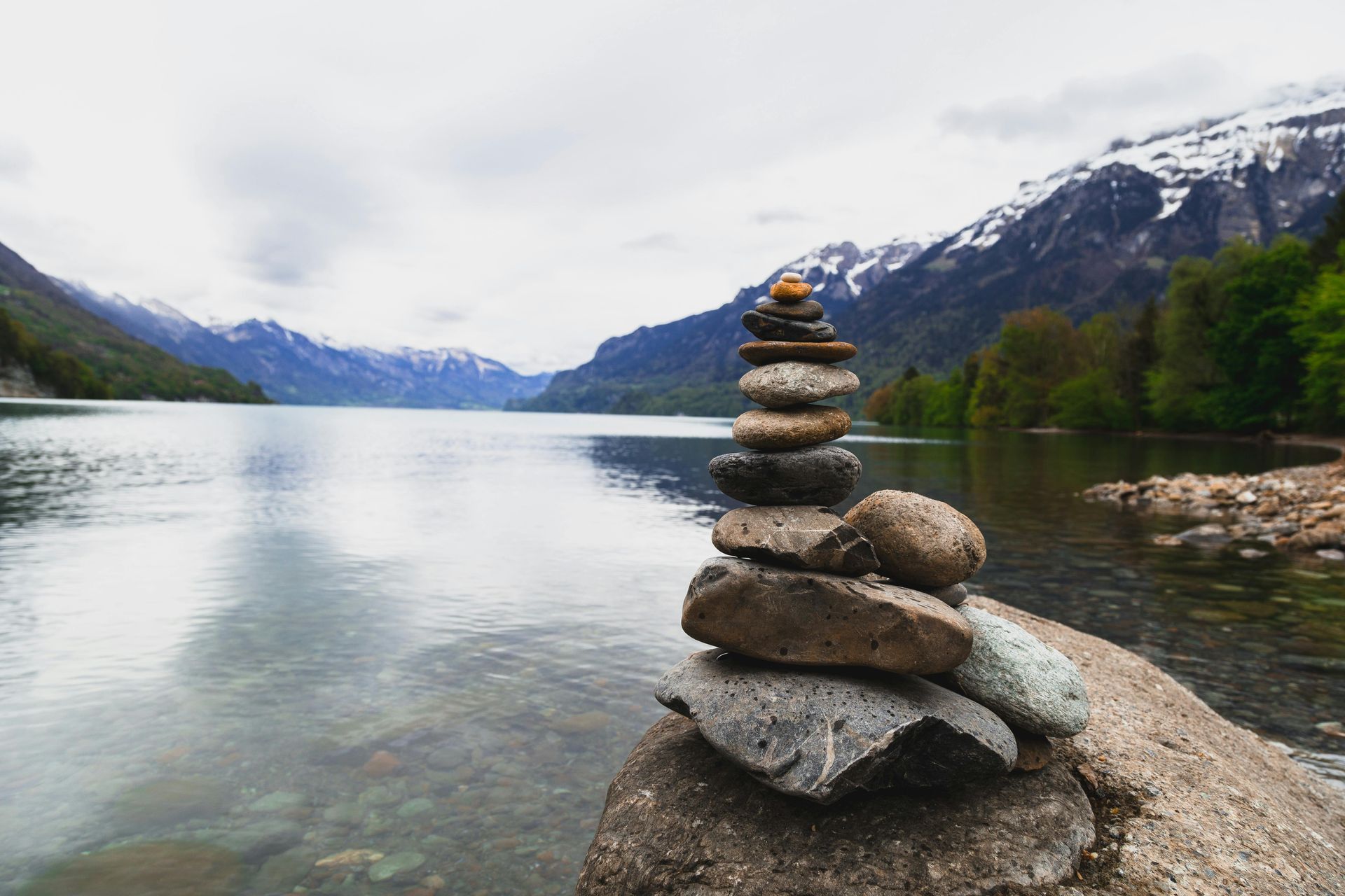 Stack of stones on a large rock by a lake, with mountains in the background.
