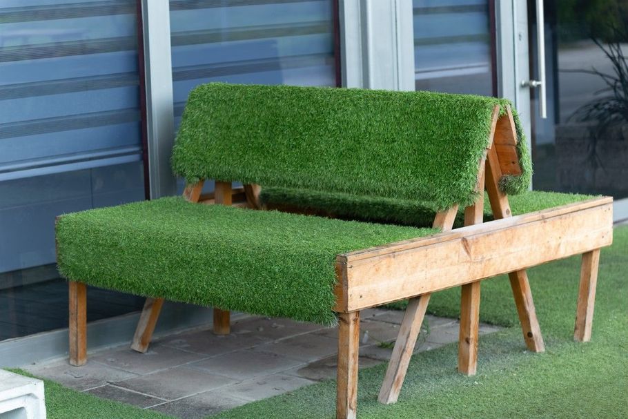Grass-covered bench and chair sculpture made of wood outdoors against a metal wall