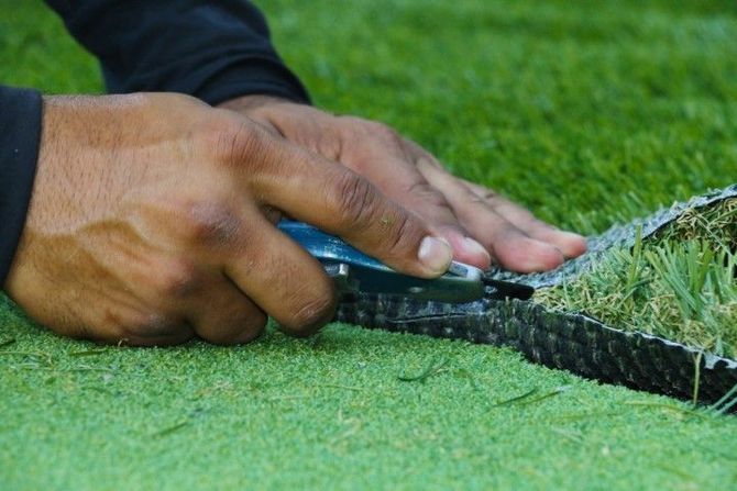Hands using a tool to trim artificial turf along its edge on a green field