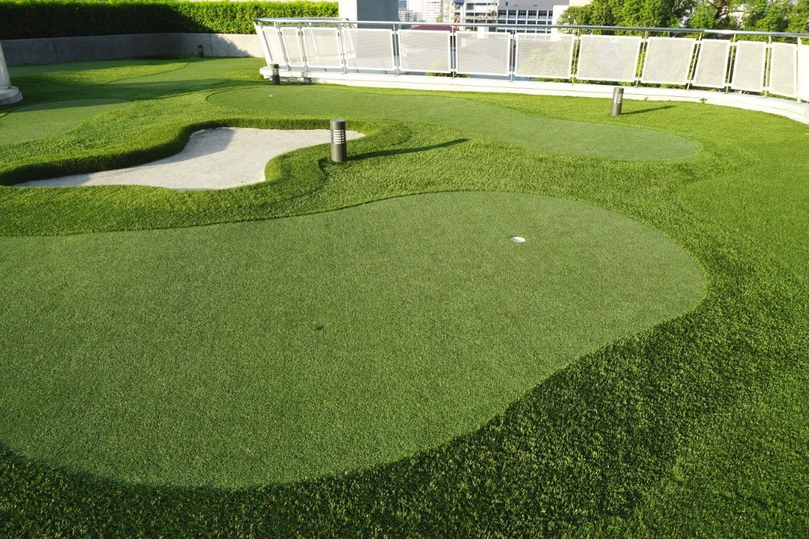 Manicured green lawn with curved walkways, a small post, and a fenced background in sunlight