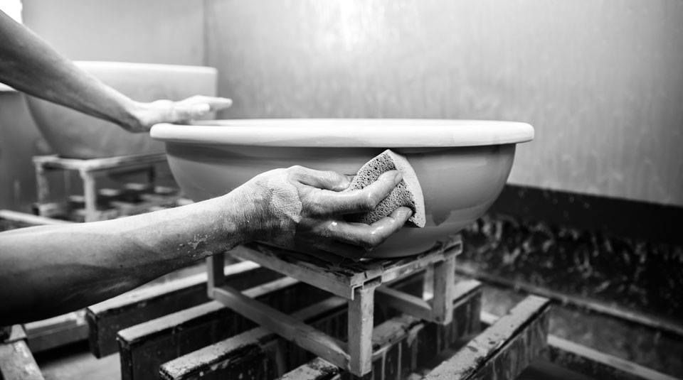 Mani che puliscono una ciotola di ceramica su un supporto di legno in un laboratorio, in bianco e nero.