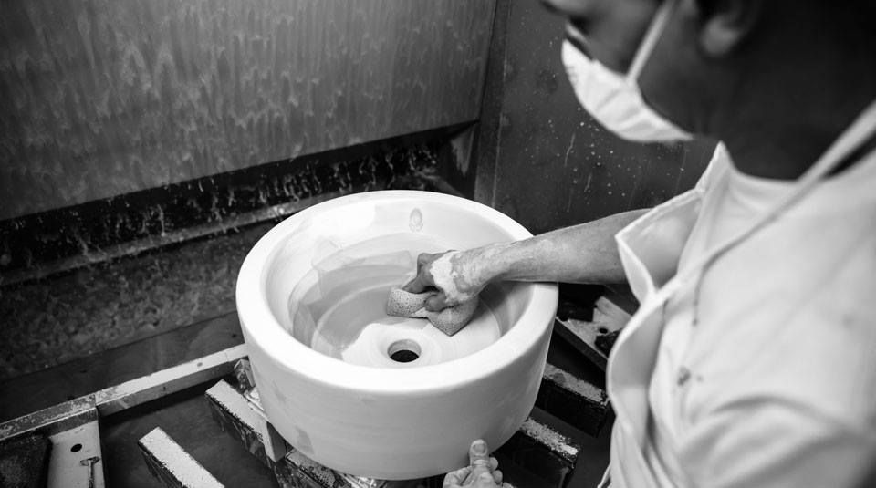 Persona con camice e mascherina che pulisce un oggetto bianco e circolare all'interno di un'area di lavoro.