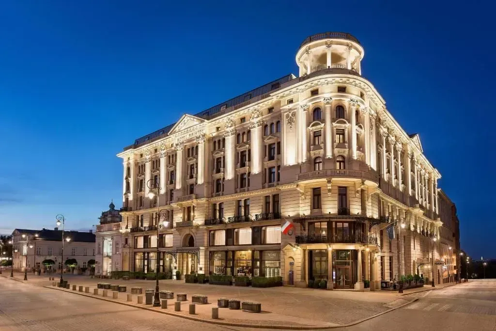 Elegante hotel illuminato, Varsavia, Polonia, con dettagli architettonici come una cupola sul tetto e la bandiera polacca.
