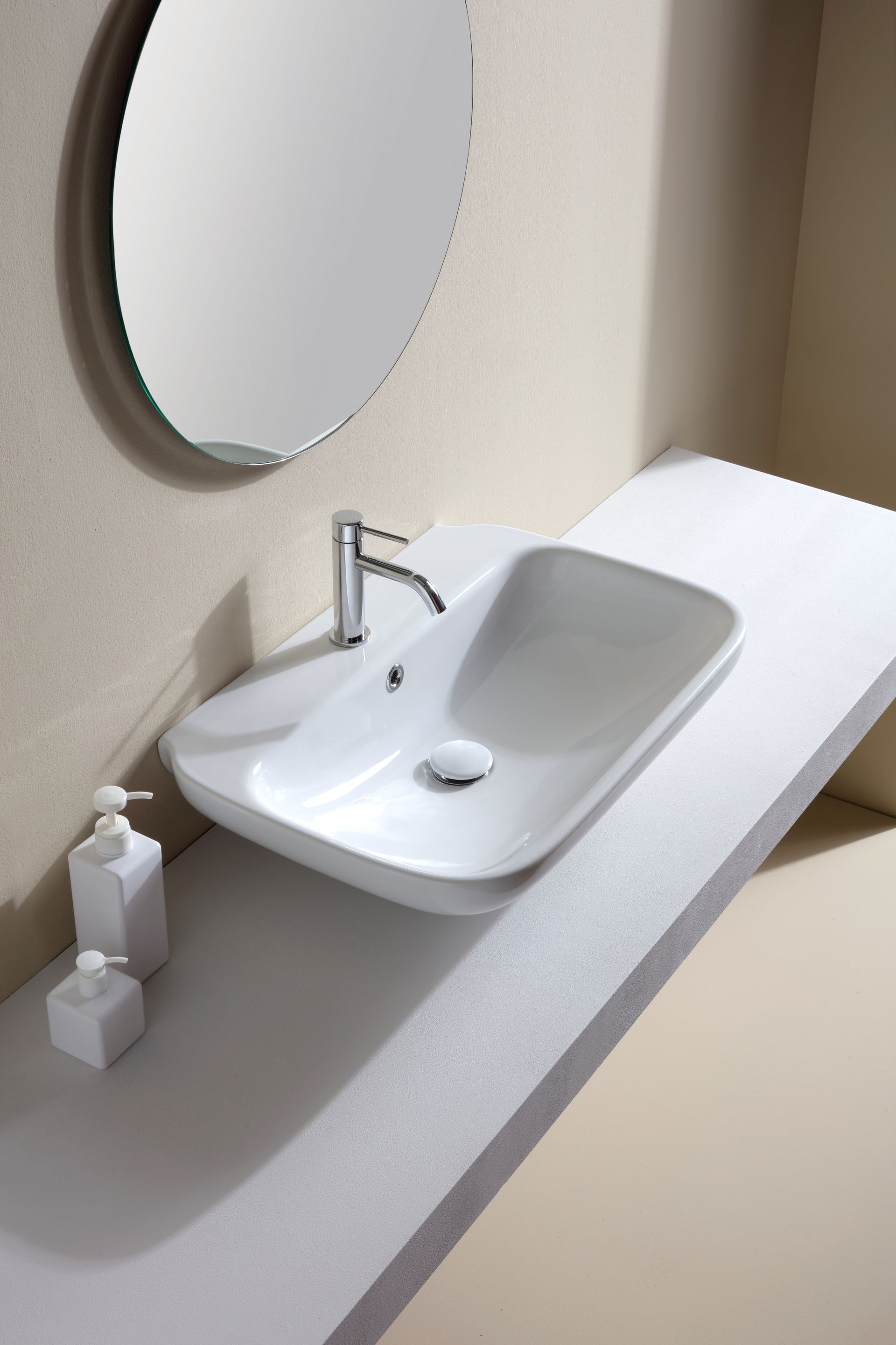 Lavandino rettangolare bianco con rubinetto cromato, su un piano di lavoro bianco con specchio rotondo e porta sapone