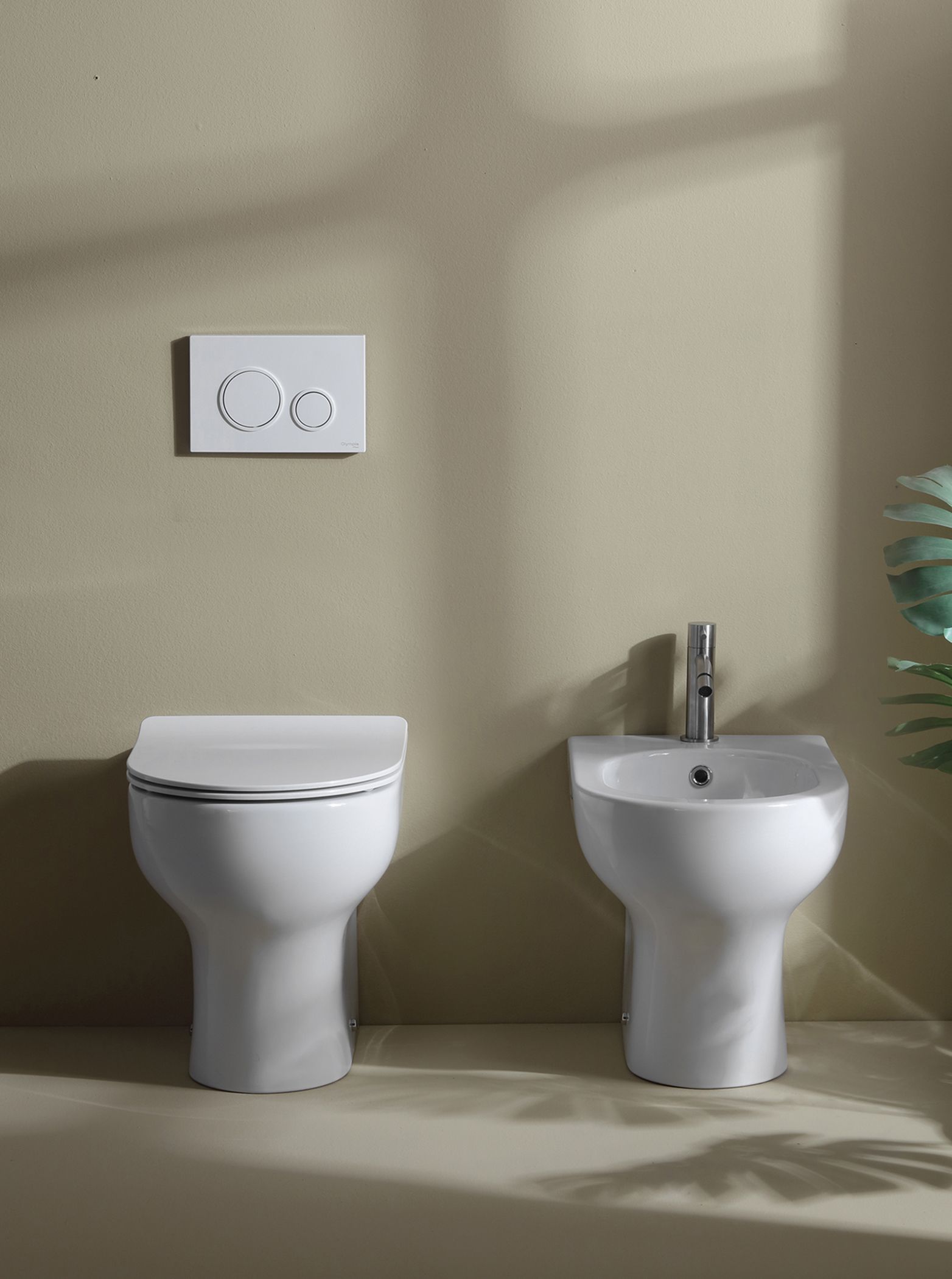 WC e bidet bianchi uno accanto all'altro contro una parete beige, con un pulsante di scarico sopra il WC.