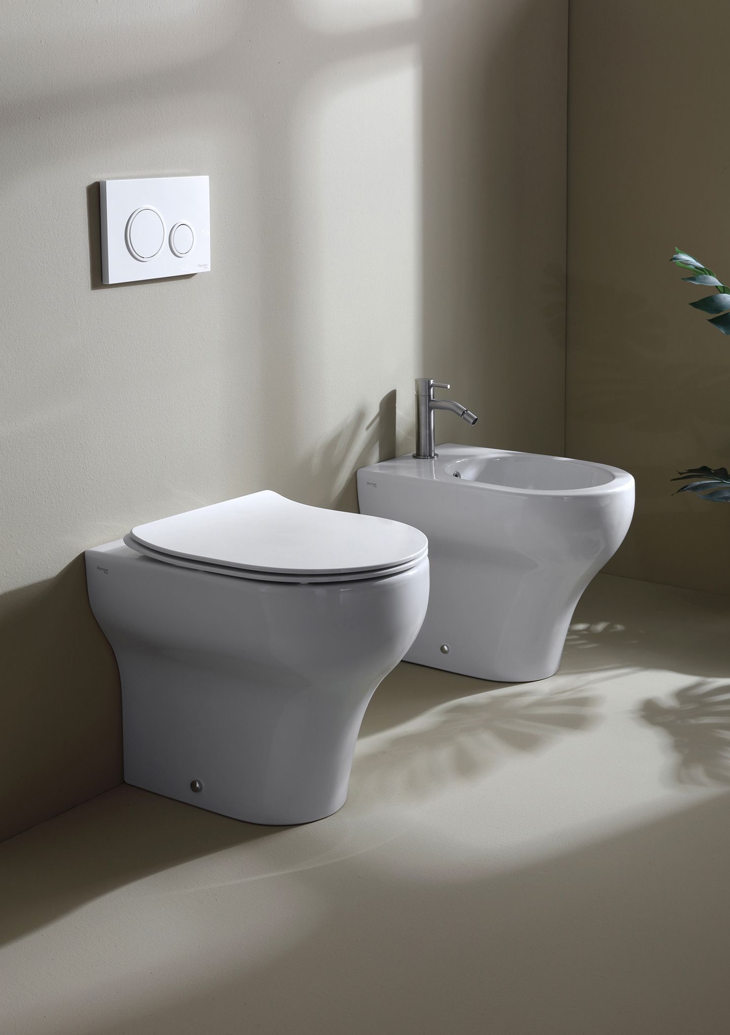 WC e bidet bianchi sospesi in un bagno con piastra di scarico e rubinetto.