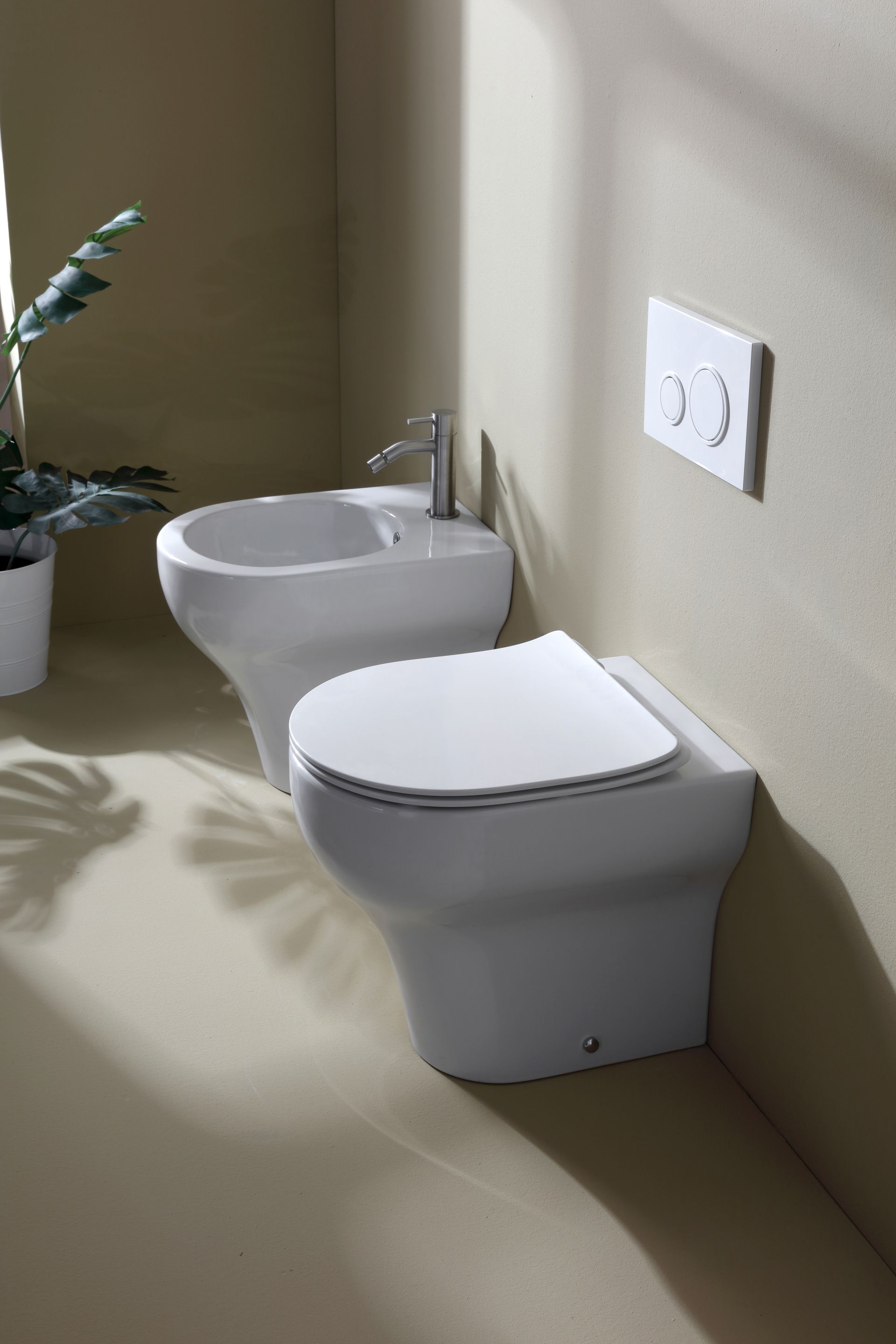 WC e bidet bianchi in un ambiente bagno, con pulsante di scarico a parete.