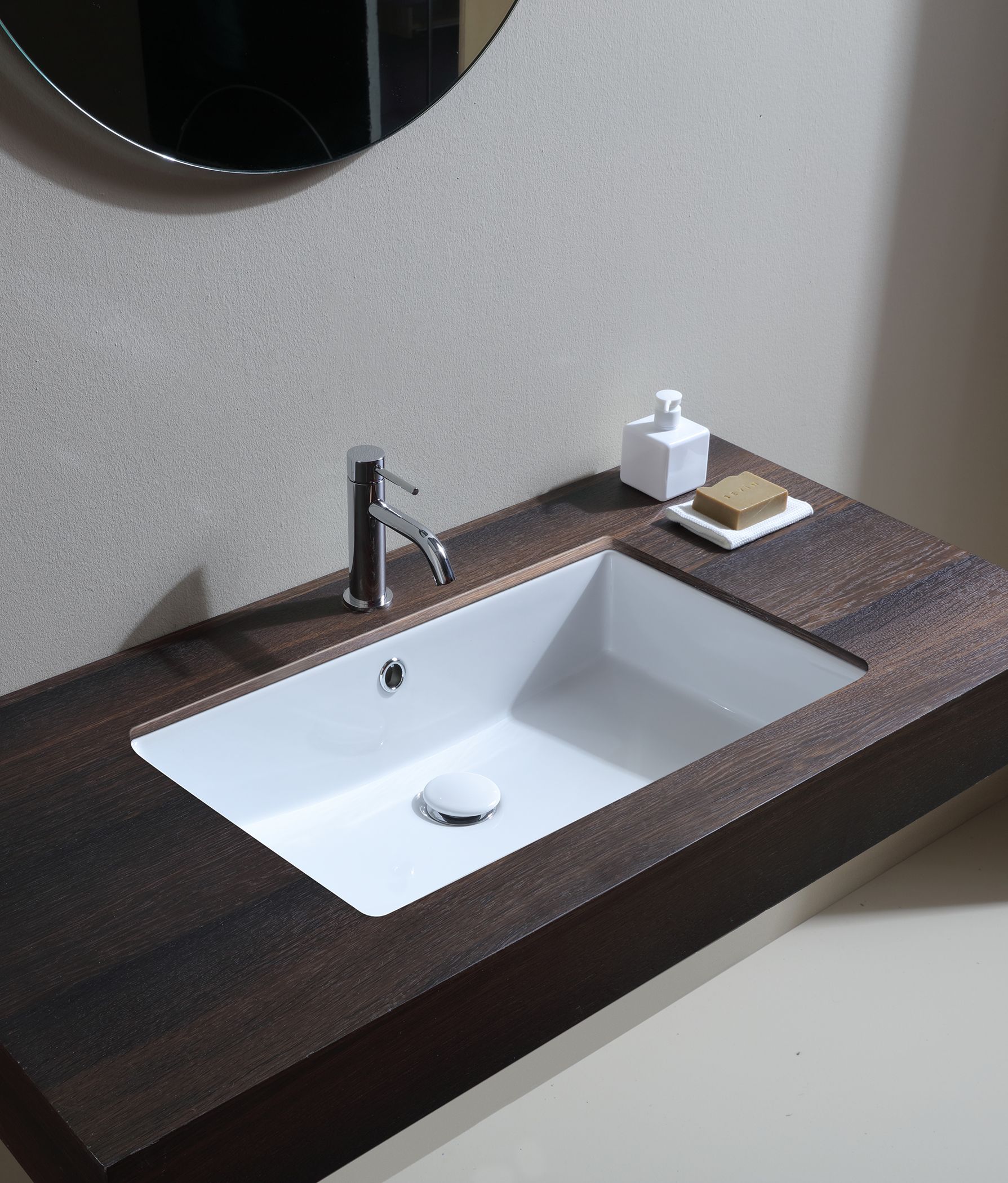 Mobile bagno con lavandino rettangolare bianco, piano di lavoro in legno scuro, rubinetto cromato e dispenser per il sapone.