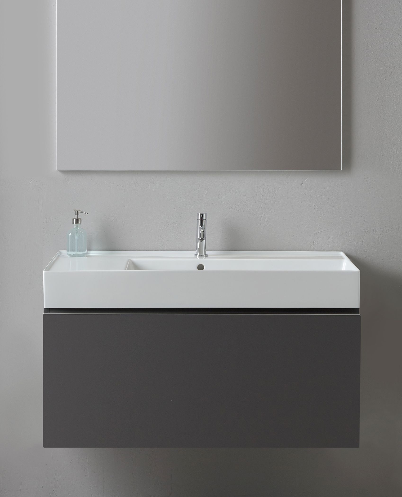 Mobiletto moderno da bagno a parete con lavandino bianco, mobile grigio, rubinetto argentato e specchio.