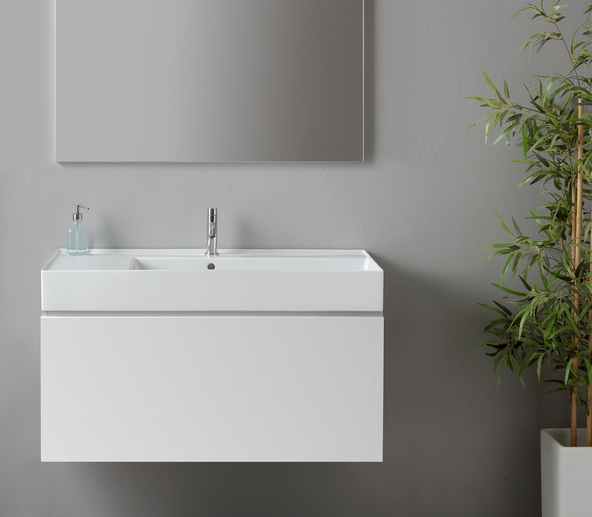Mobile bagno sospeso bianco con rubinetto, specchio e pianta.